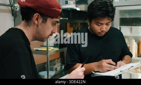Chefs checking order details in dark kitchen managing food delivery workflow Stock Photo