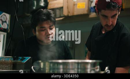 Professional chefs working in a busy dark kitchen, preparing food with steam rising Stock Photo