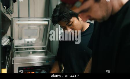Professional chefs preparing food using a vacuum sealing machine in a dark kitchen Stock Photo