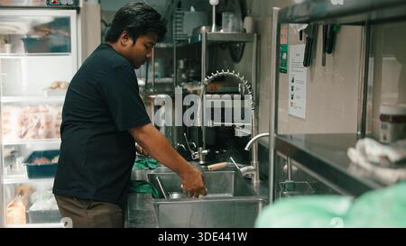 Chef washing dishes in a commercial dark kitchen, working at stainless steel sink Stock Photo