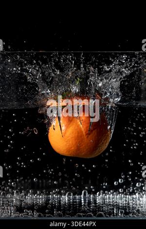 A mandarin falls into a container full of water, raising a large splash Stock Photo