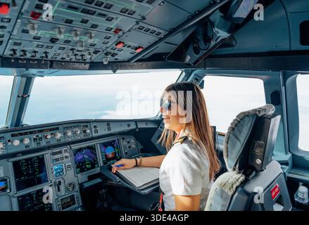 Happy female pilot smiling inside aircraft cockpit in flight Stock Photo