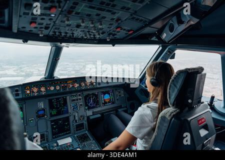 Female pilot operating commercial aircraft cockpit during landing Stock Photo