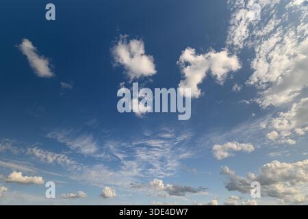 A beautifully tranquil sky filled with soft, fluffy clouds gently floating in a vivid and bright blue backdrop Stock Photo
