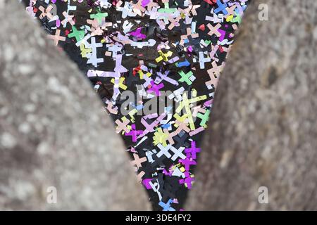 Colorful triangular gap filled with festive shiny cross confetti showing joyful celebration spirit between rough gray stone concrete borders creating Stock Photo