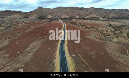 Aerial view of a lonely highway cutting through a vast, arid landscape under a moody sky, framed by distant mountains, Fruita, Colorado, United States Stock Photo