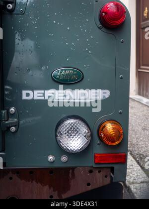 Close-up view of the iconic Land Rover Defender emblem and taillights on a wet, dark green vehicle exterior Stock Photo