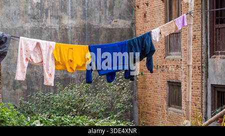 Colorful clothing hangs on a laundry line strung between two brick walls in an urban environment, depicting daily life and vibrant simplicity. Stock Photo