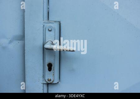 Rusted metal door handle on a blue industrial door, emphasizing age, texture, and urban character Stock Photo