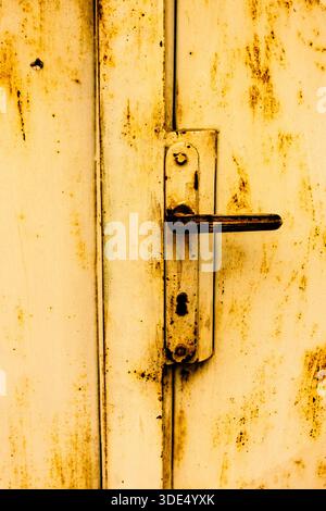 Rusted metal handle on a yellowed industrial door, highlighting corrosion and gritty texture Stock Photo