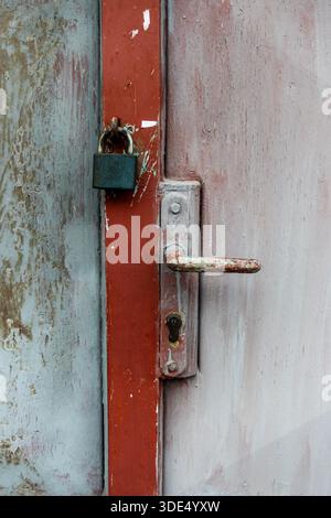 Old padlock securing a red and grey metal door, showing rust, wear, and industrial security Stock Photo