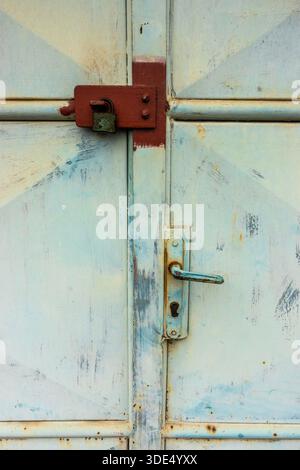 Old padlock securing a metal door, showing rust, wear, and industrial security Stock Photo