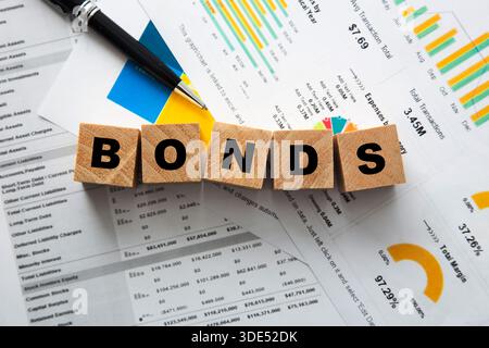 Wooden blocks spelling bonds with financial charts, graphs, and a pen on economic reports Stock Photo