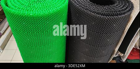 Close-up view of two coiled plastic anti-slip mats standing upright. One mat bright green, other mat dark grey. Mats present textured surface with gri Stock Photo
