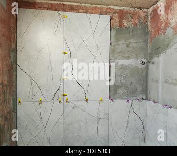 View of interior renovation with new marble effect ceramic tiles installed on wall using leveling system clips for precise alignment and flat surface, Stock Photo