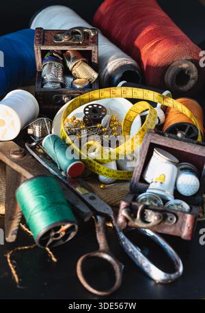 Spools of thread of various colors, Thimbles in small wooden treasure chest, Steel scissors, Sewing needles stuck in a green miniature spools thread a Stock Photo