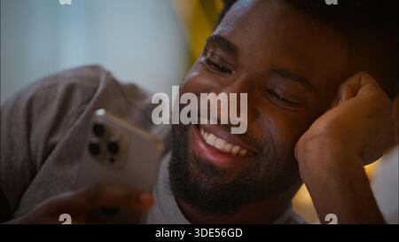 Happy laughing cheerful customer client male user African American man guy holding mobile phone browsing cellphone smartphone technology playing game Stock Photo