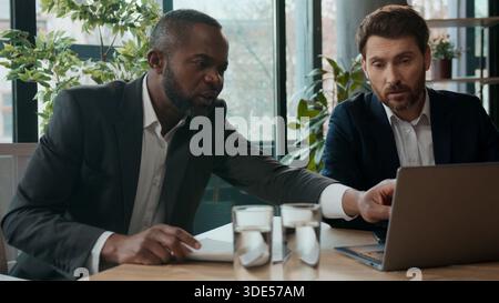 Two multiethnic company men workers business team busy with online project diversity employers multiracial businessmen discussing deals task in office Stock Photo