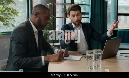 Serious business men multiracial team with laptop talking problem working computer documents Caucasian manager man showing African American male boss Stock Photo