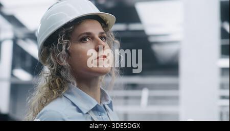 Close Up Female Technical Specialist Wearing Shirt and ID Badge, Overseeing Robotic Assembly Process in Clean, Modern Plant in Safety Helmet. Concept of Safety Protocols in Advanced Automation. Stock Photo
