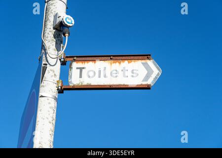 Old and faded public toilets sign against blue sky Stock Photo
