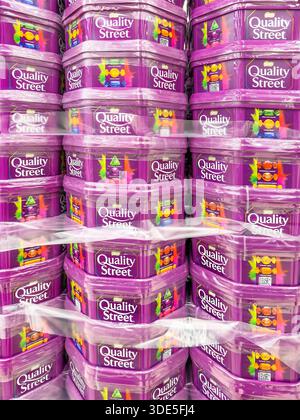 Stacks of Quality Street chocolate plastic tubs wrapped in plastic film on a store display shelf ready for sale at christmas tesco store uk Stock Photo