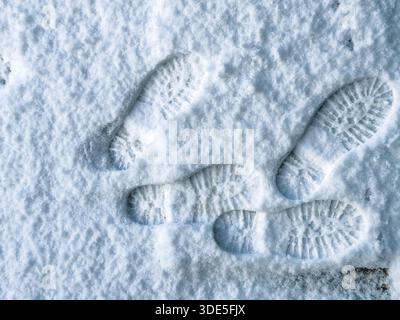 Multiple boot prints in freshly fallen snow showing deep tread patterns and overlapping footsteps on a cold winter frozen surface Stock Photo