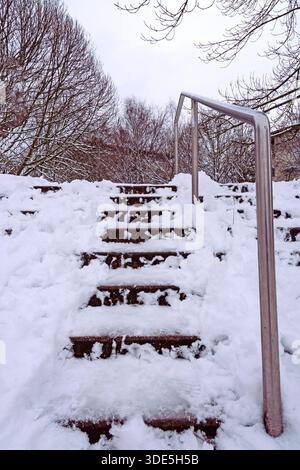 Captured in a vertical composition, icy snow-covered stairs lead upward while a metal handrail serves as a strong leading line, symbolizing winter cha Stock Photo
