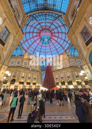 Milan. Italy. A towering Christmas tree adorned with lights stands in the center of a bustling shopping arcade, surrounded by ornate architecture and Stock Photo