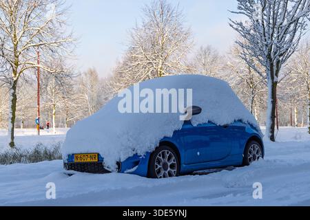 Small blue car parked on the side of the road completely buried under a thick layer of white snow during a sunny winter day. Stock Photo