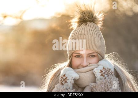 Portrait of young cute woman at sunny winter day. Female in warm clothes smiling, looking at camera Stock Photo