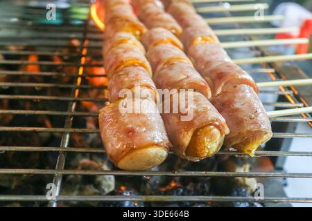 Bacon wrapped sausages grilling over hot charcoal, highlighting smoky barbecue texture, outdoor cooking style, and indulgent comfort snacks. Stock Photo