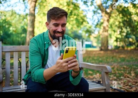 Happy man smiling using yellow smartphone in park Stock Photo