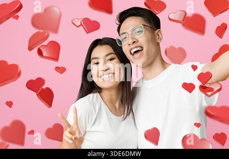 Cute Asian Couple Enjoys Taking Selfie Against Yellow Background Filled With Hearts Stock Photo