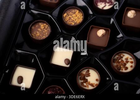 close-up of assorted gourmet chocolates and truffles in a glossy black plastic box tray, featuring milk, dark and white fillings topped with caramel, Stock Photo