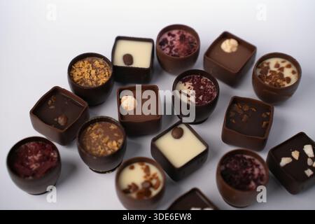 assorted artisanal chocolate bonbons and pralines arranged on a soft pale backdrop, glossy dark and white fillings topped with nuts, caramel and dried Stock Photo