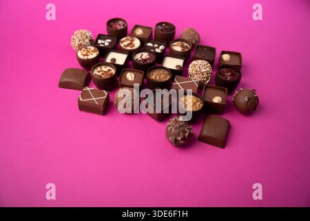 assorted artisanal chocolate bonbons and truffles arranged on a bright magenta-pink tabletop backdrop, showcasing glossy and textured pralines, ganach Stock Photo