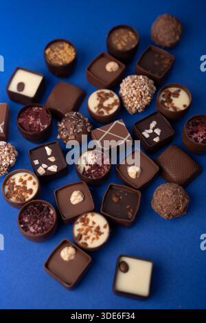 close-up photograph of assorted artisanal chocolate pralines, bonbons and truffles arranged on a vivid cobalt-blue surface, highlighting glossy ganach Stock Photo