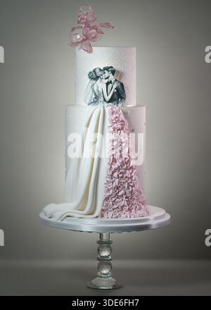 Tall luxury wedding cake decorated with a romantic couple silhouette, intricate damask patterns, pink wafer paper flowers, and a textured ruffle train Stock Photo