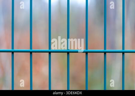 Blue coated metal fence bars forming a grid pattern with a blurred background Stock Photo