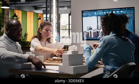 Team members work together in office with architectural software and 3D models to envision a successful residential property with smart city infrastructure goals. Urban development. Stock Photo