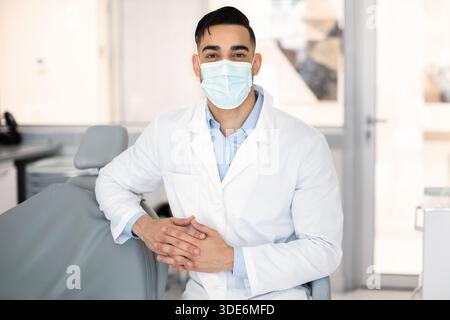 Portrait Of Young Middle-Eastern Dentist Wearing Protective Medical Mask Posing At Workplace Stock Photo