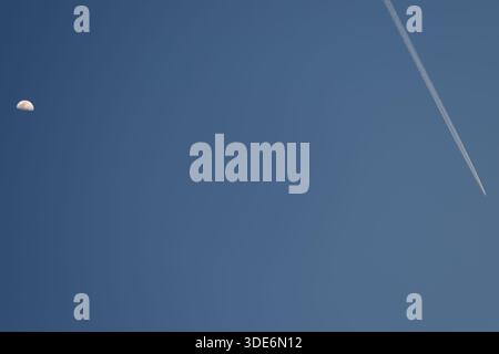 Half moon and airplane contrail appearing in a vast clear blue sky Stock Photo