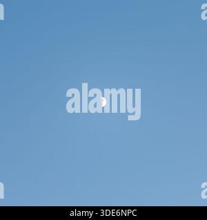 Half moon appearing in clear blue sky during daylight Stock Photo