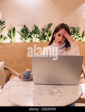 Woman suffering headache using laptop in remote workspace Stock Photo