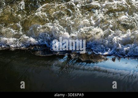 Water rushing over a barrier creating white foam and a dynamic surface Stock Photo
