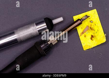 Soldering iron, desoldering pump, and a dirty sponge laying on a dark surface Stock Photo