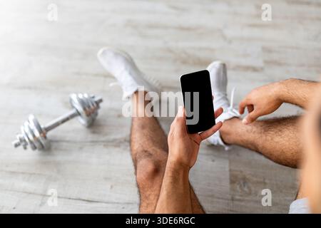 Cropped view of fit young guy with dumbbell checking new app on mobile phone during break, mockup for design Stock Photo