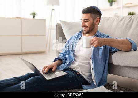 Smiling jewish man watching video on computer, drinking coffee Stock Photo