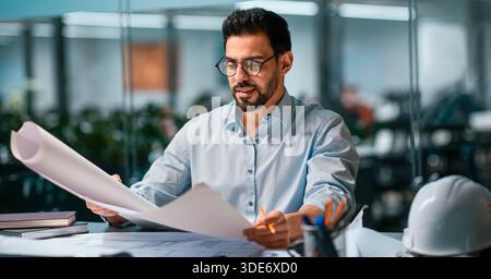 Man Reviewing Construction Plans in a Modern Office Setting During Daytime Hours Stock Photo